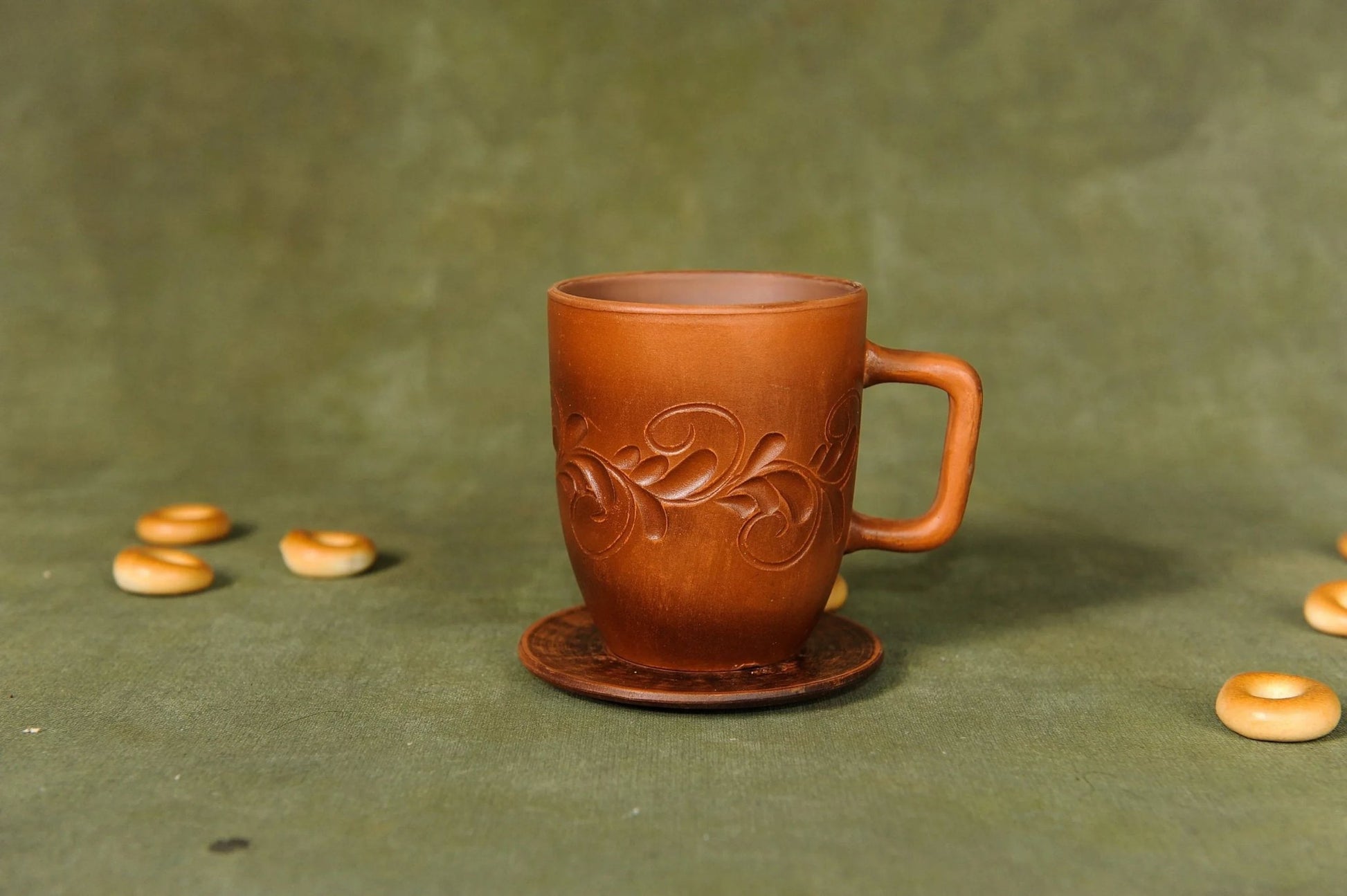 Handcrafted ceramic clay cup with plate and embossed design on green background, clayproductsshop