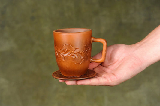 Hand holding a handmade ceramic clay cup with floral relief design on matching plate