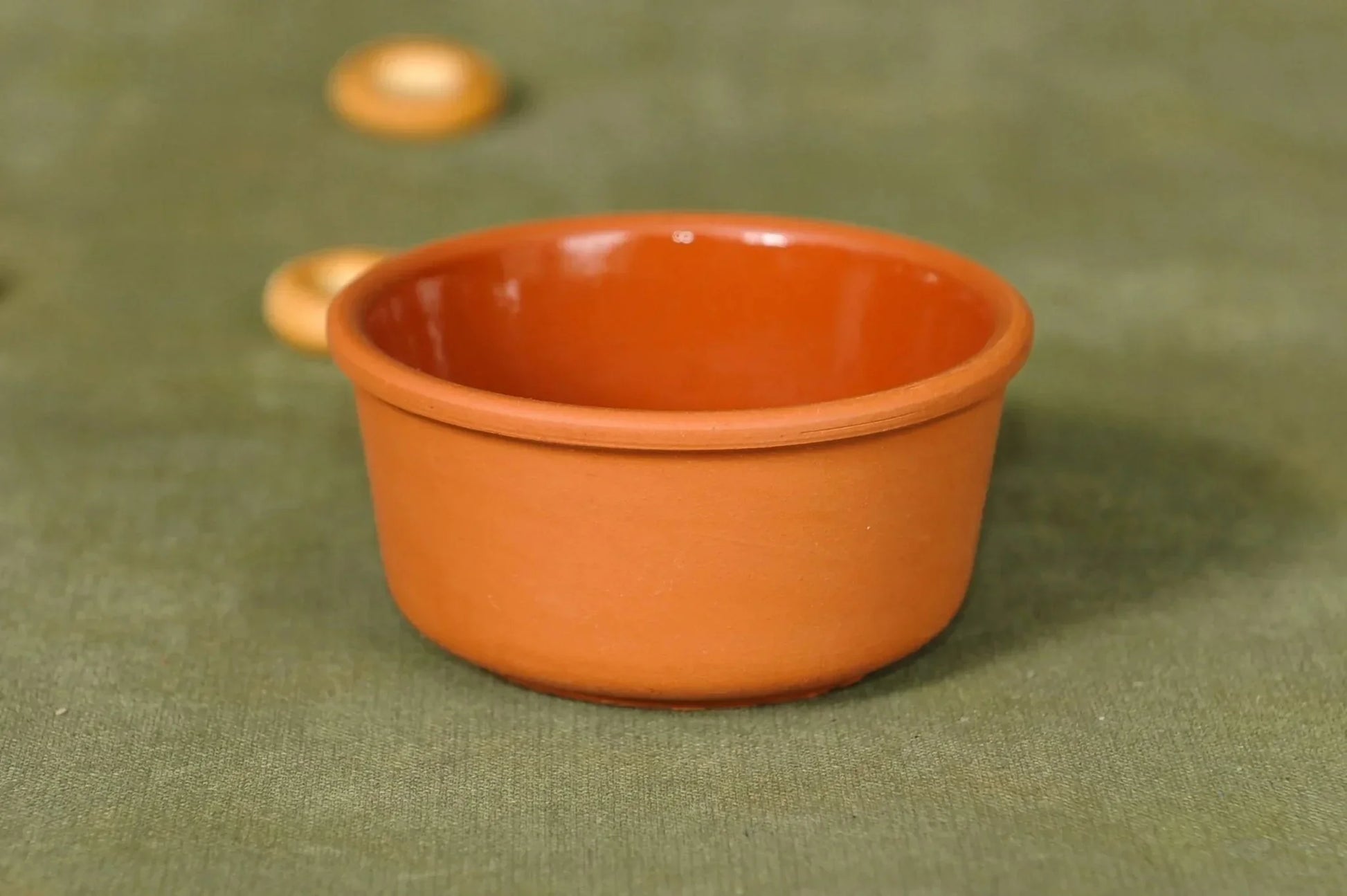 Handmade terracotta clay bowl with smooth finish on green fabric background