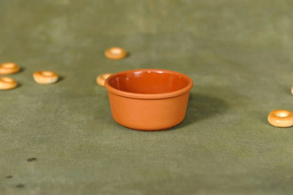 Handmade terracotta clay bowl on green fabric, surrounded by small round pastries