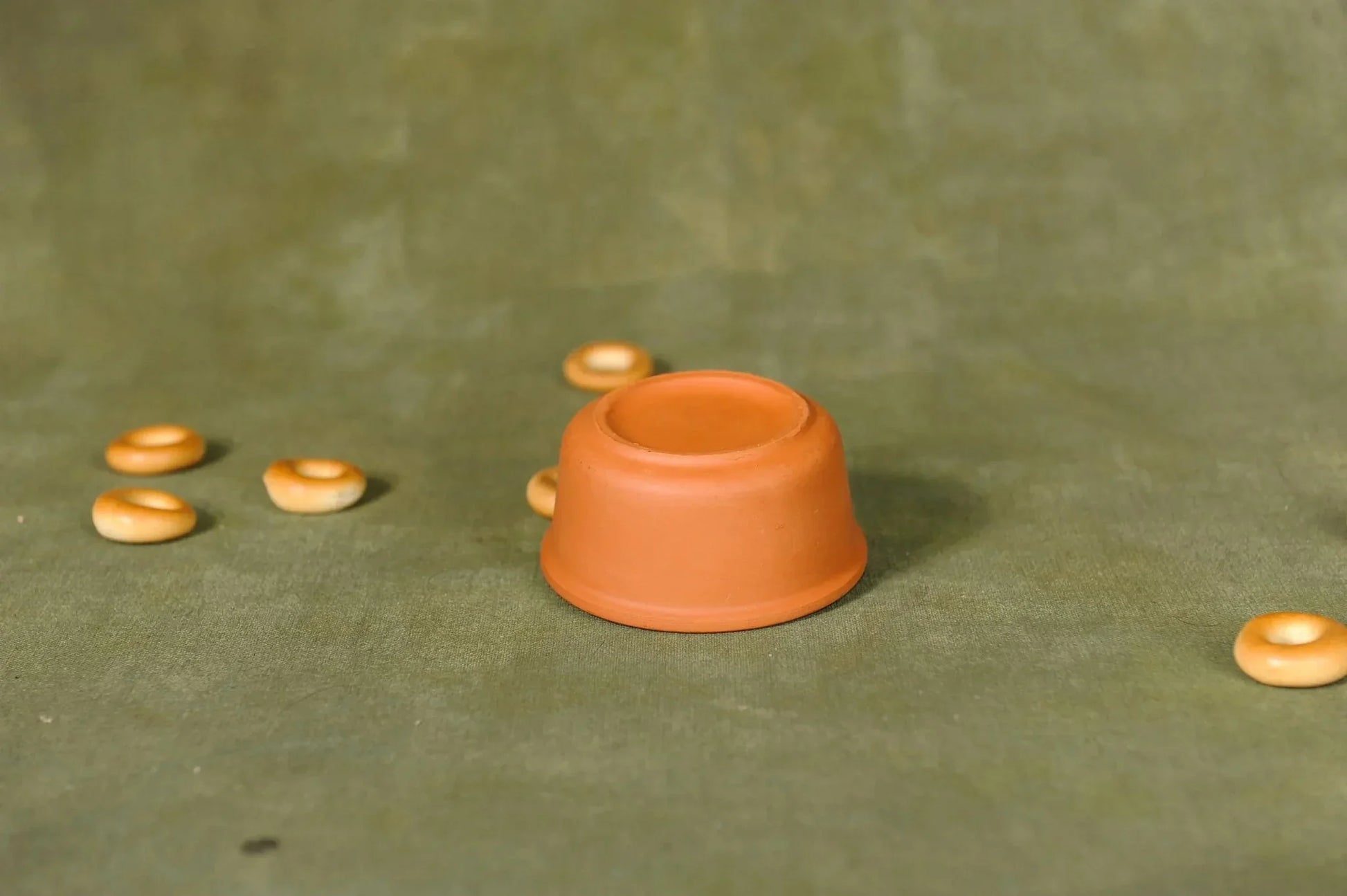 Handmade terracotta clay cupcake mold on green fabric with small round pastries