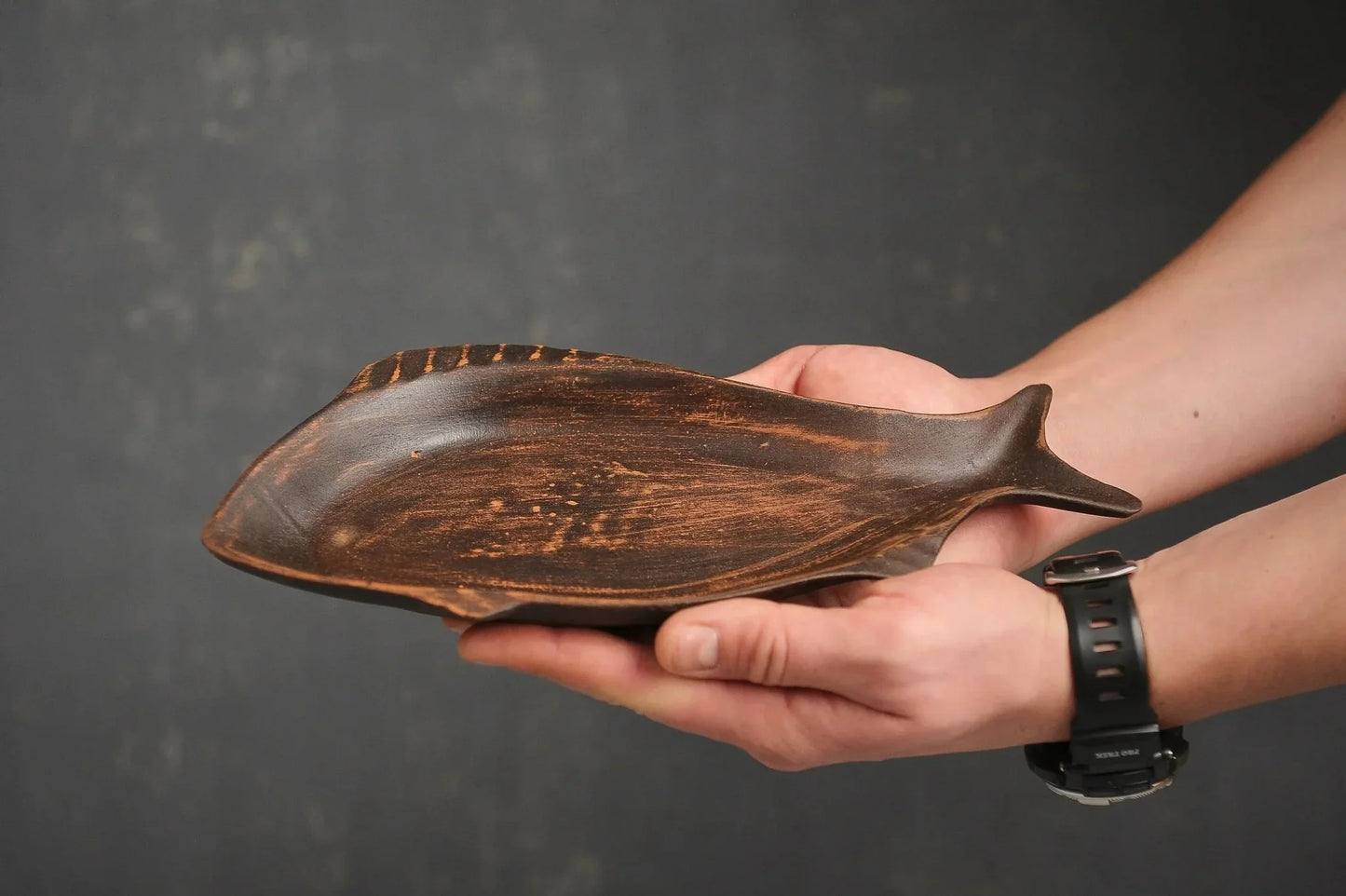 Hand holding a handcrafted ceramic fish plate, rustic clay dish from clayproductsshop