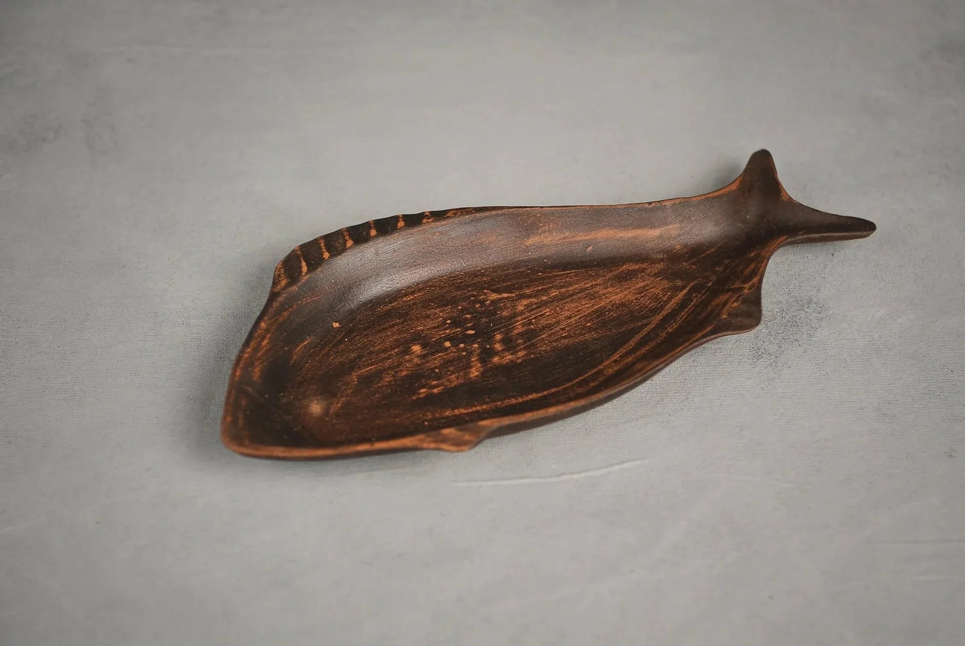 Handcrafted ceramic fish-shaped clay plate on gray background, artisan home décor