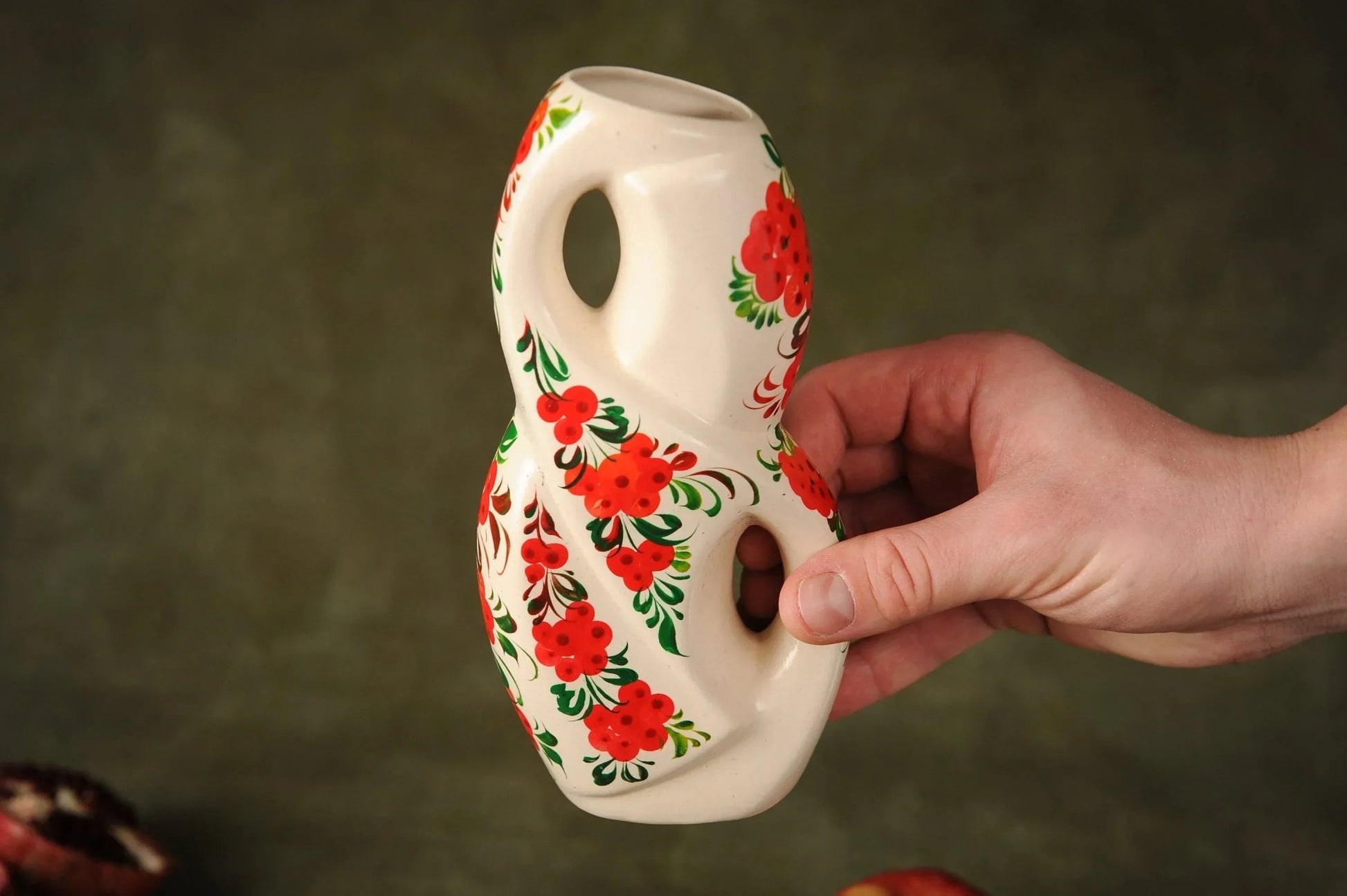 Hand holding a unique white clay ceramic vase with red floral design, artisan home décor.