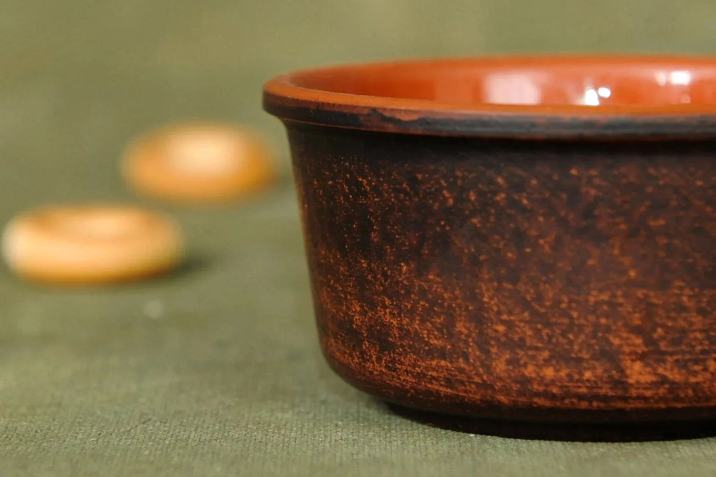Handmade clay bowl with rustic brown finish on green fabric, artisan pottery homeware