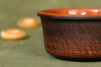 Handmade clay bowl with rustic brown finish on green fabric, artisan pottery homeware