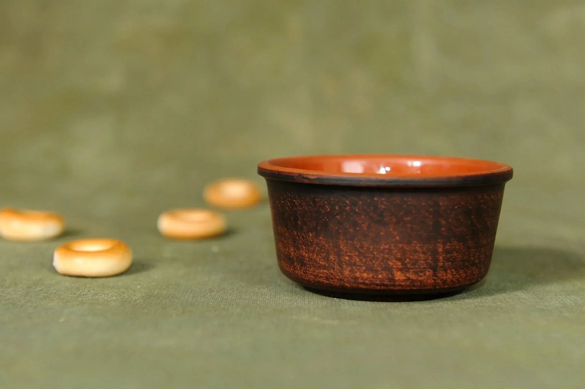 Handmade clay bowl, small brown pottery cup, artisan homeware on green fabric background