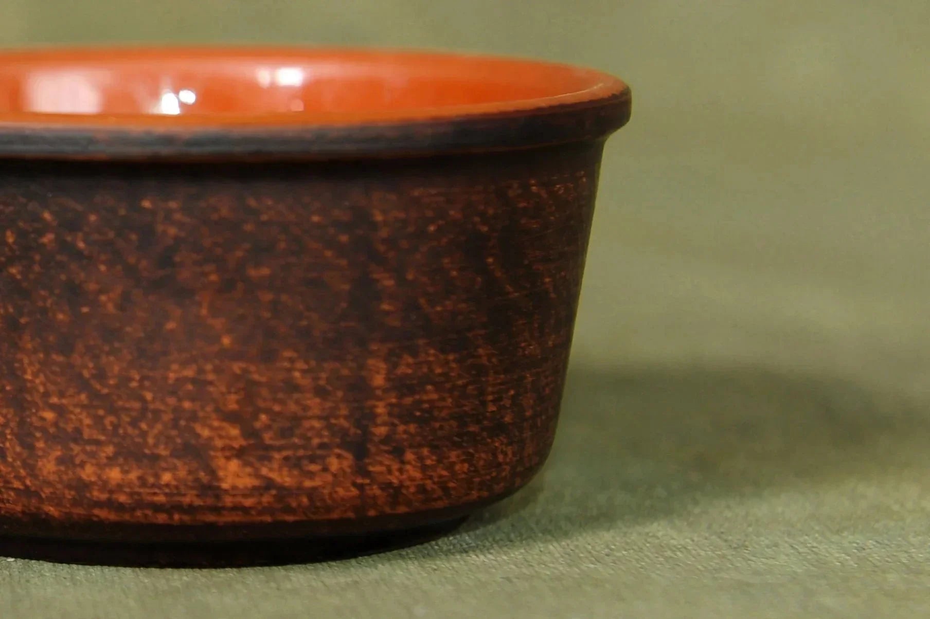 Handcrafted clay bowl with brown textured exterior and smooth orange interior on fabric surface