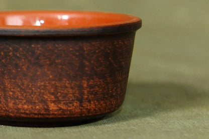 Handcrafted clay bowl with brown textured exterior and smooth orange interior on fabric surface