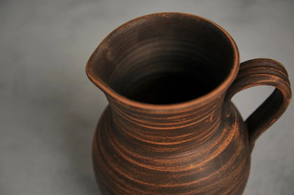 Handmade brown ceramic milk jug with handle on gray background, artisan clay homeware
