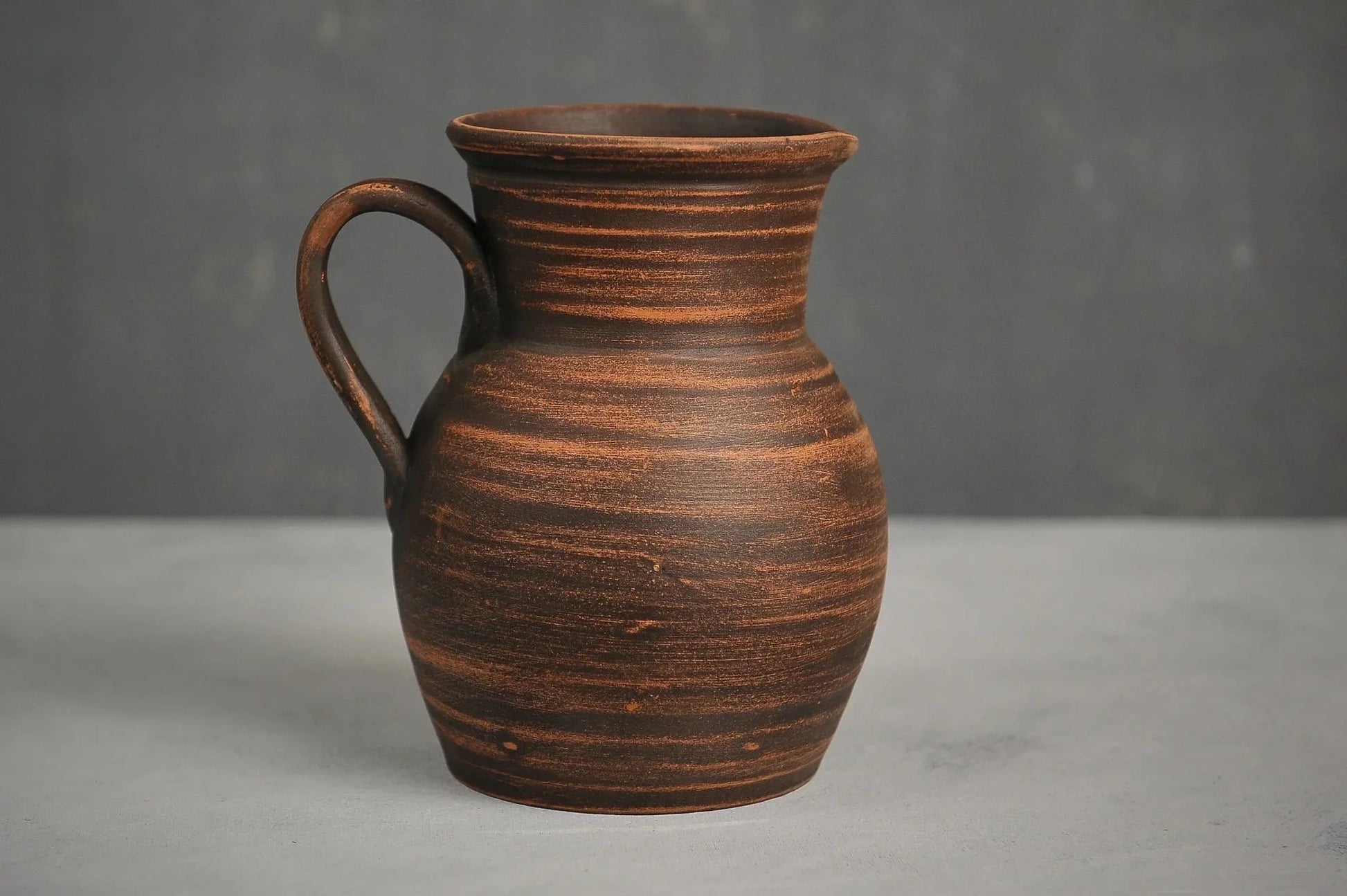 Handmade ceramic milk jug with handle, rustic brown clay pitcher on neutral background