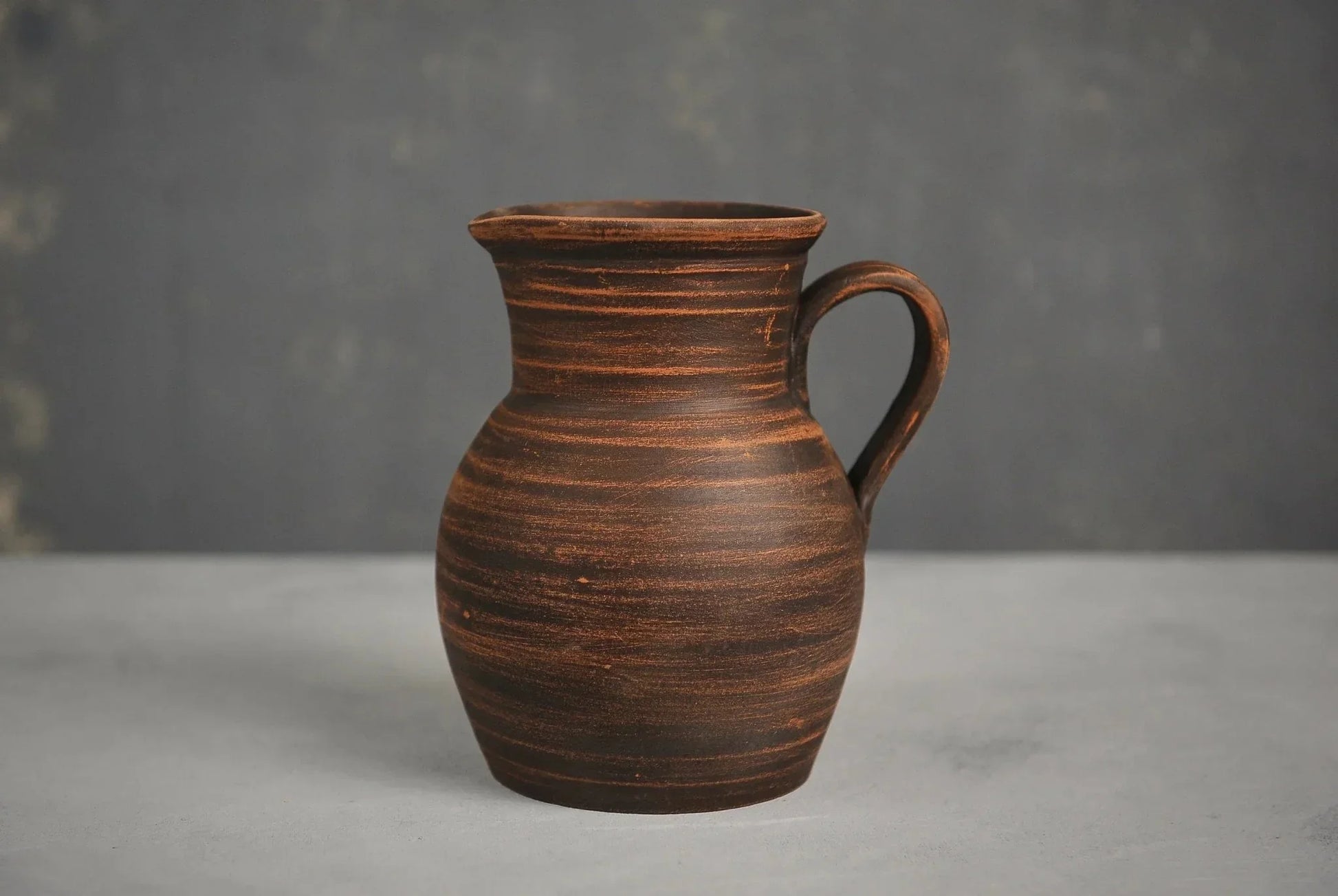 Handmade ceramic milk jug with handle, rustic brown pitcher on gray background