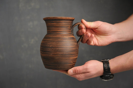 Hand holding handmade brown ceramic milk jug with handle from clayproductsshop