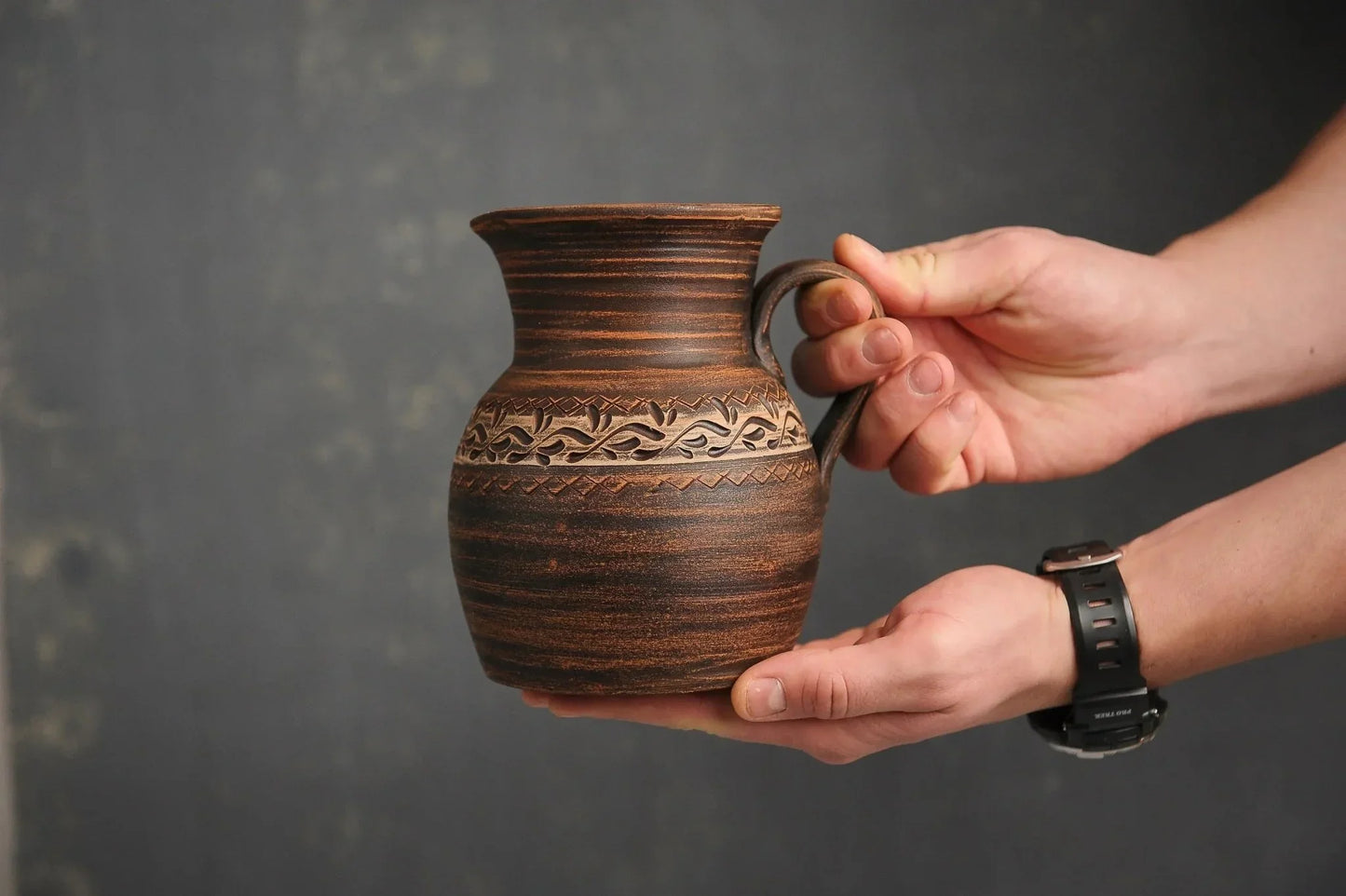 Hand holding a handmade ceramic milk pitcher with engraved patterns, clayproductsshop homeware