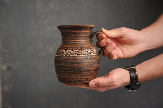 Hand holding a handmade ceramic milk pitcher with engraved patterns, clayproductsshop homeware