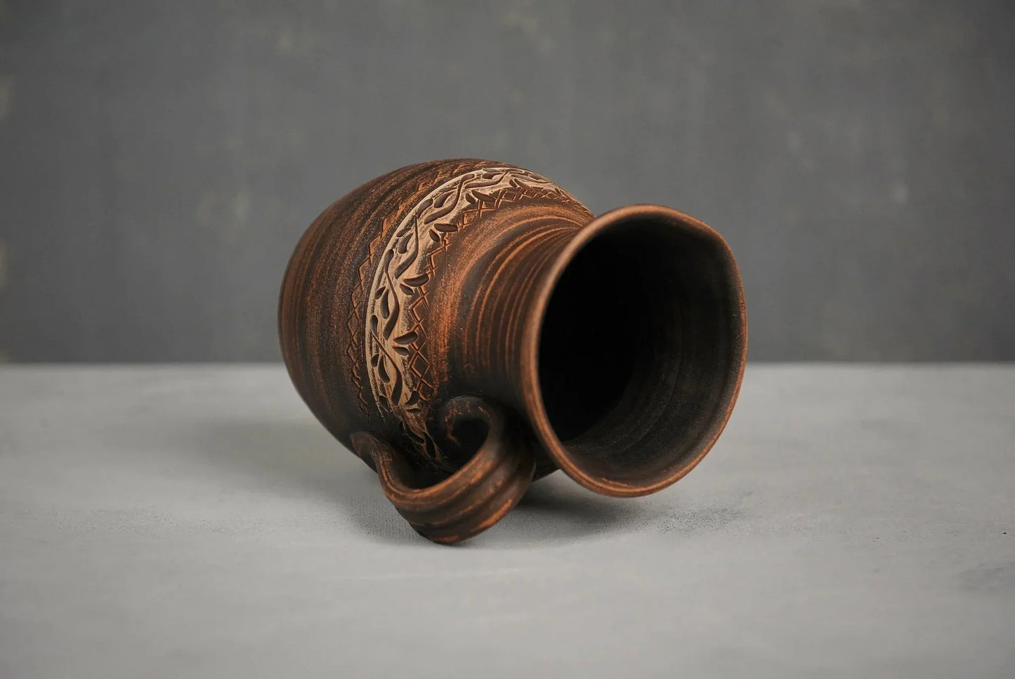 Handmade ceramic milk pitcher with hand-engraved pattern on gray surface, clay homeware