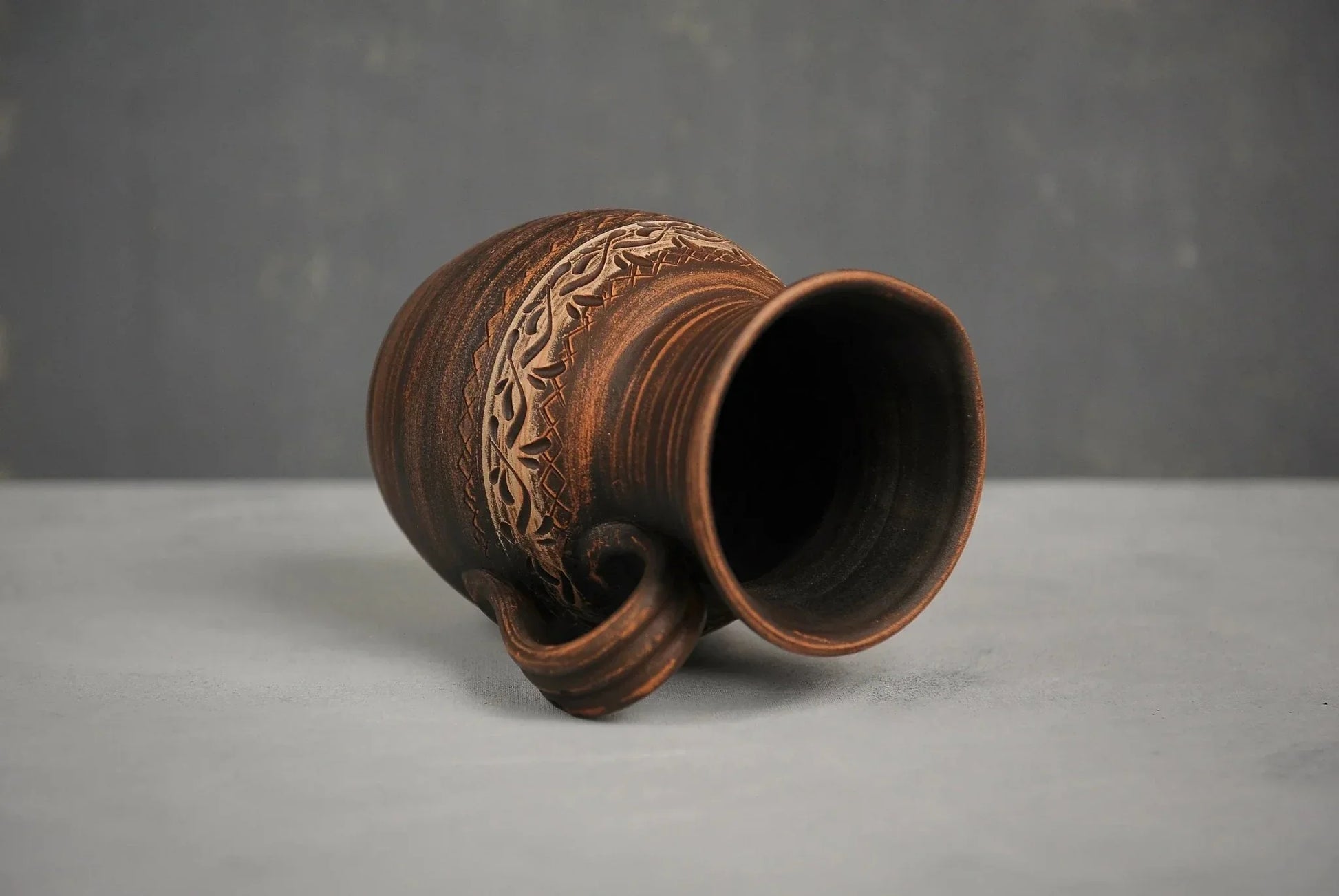 Handmade ceramic milk pitcher with hand-engraved pattern on gray surface, clay homeware