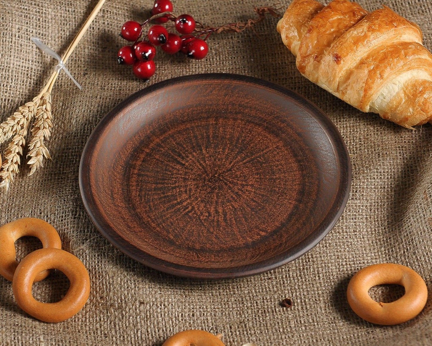 Handmade brown ceramic plate on burlap with croissant, wheat, and bagels, clayproductsshop