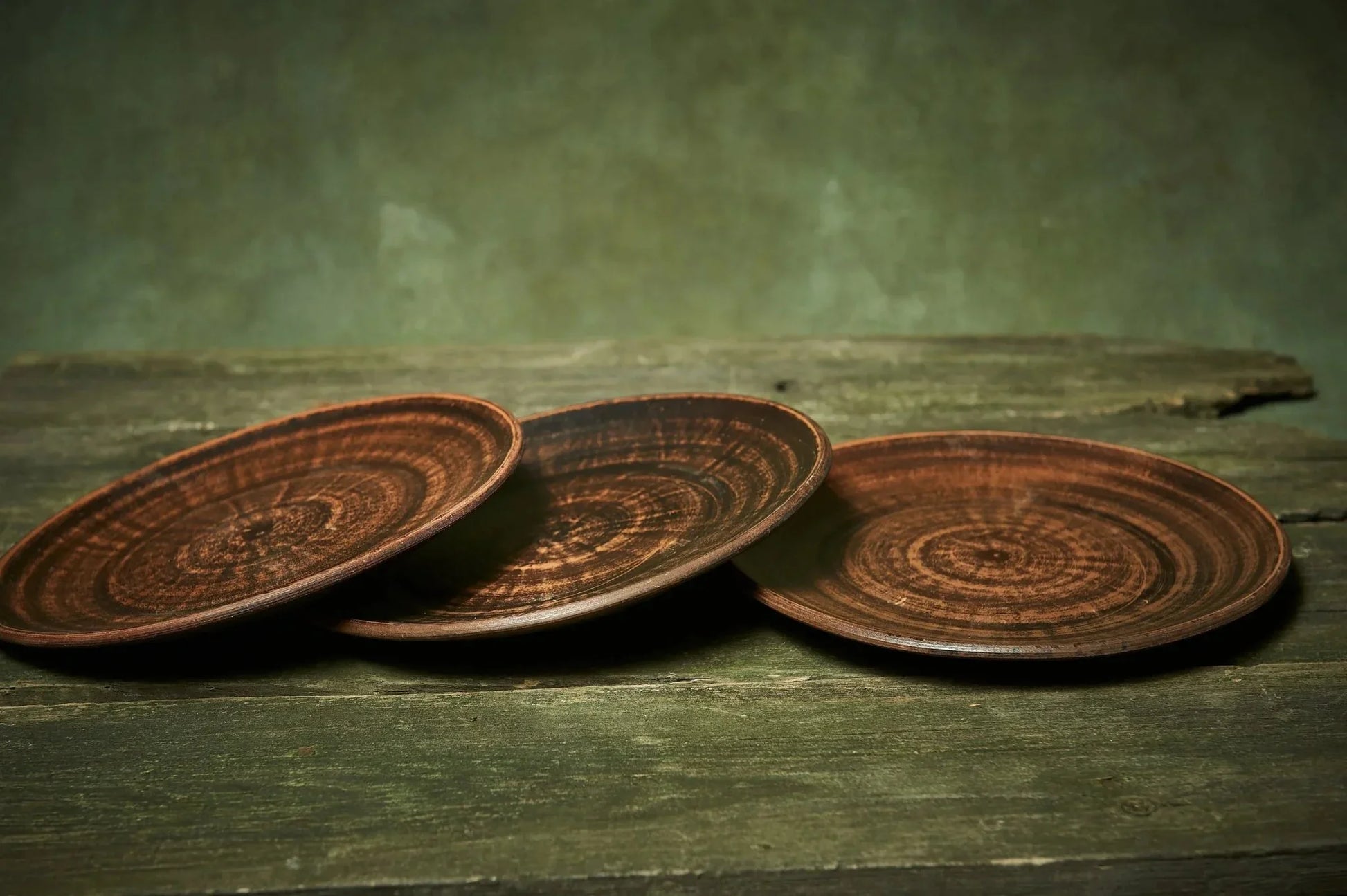 Set of three handmade ceramic plates with rustic brown glaze on a wooden table