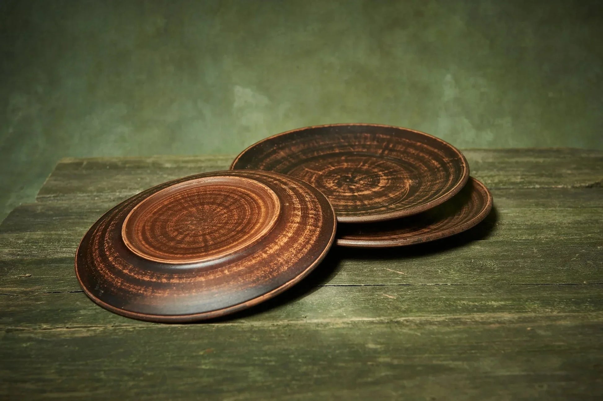 Set of three handmade ceramic plates with rustic brown finish on wooden surface