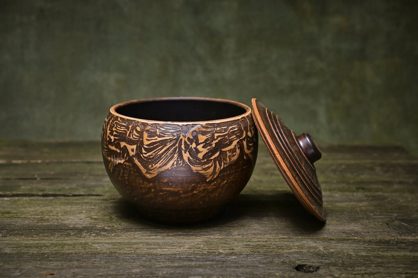 Handmade ceramic clay pot with lid on rustic wood table, artisan pottery kitchenware