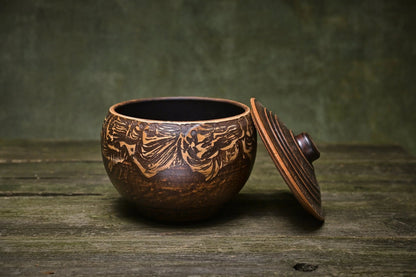 Handmade ceramic clay pot with lid on rustic wood table, artisan pottery kitchenware