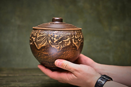 Handmade brown ceramic pot with lid, artisan clay pottery, held in hands, rustic décor
