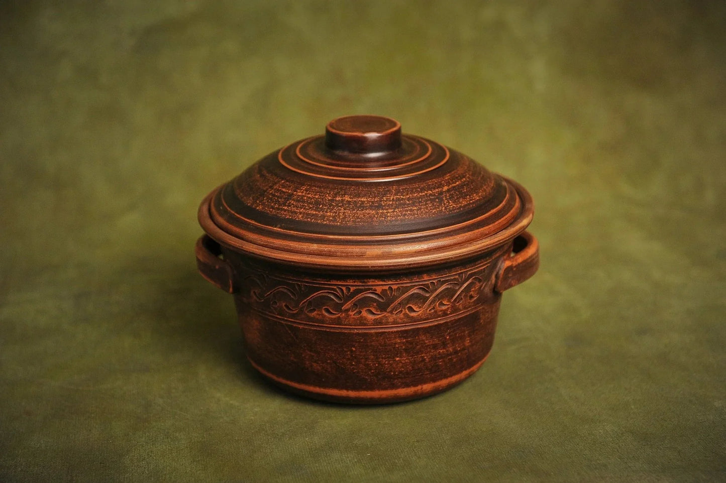 Handmade ceramic clay pot with lid and textured design, artisan kitchen cookware on green background