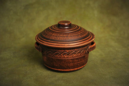 Handmade ceramic clay pot with lid and textured design, artisan kitchen cookware on green background