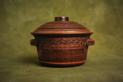 Handmade ceramic clay pot with lid, decorative handles, artisan bakeware on green background