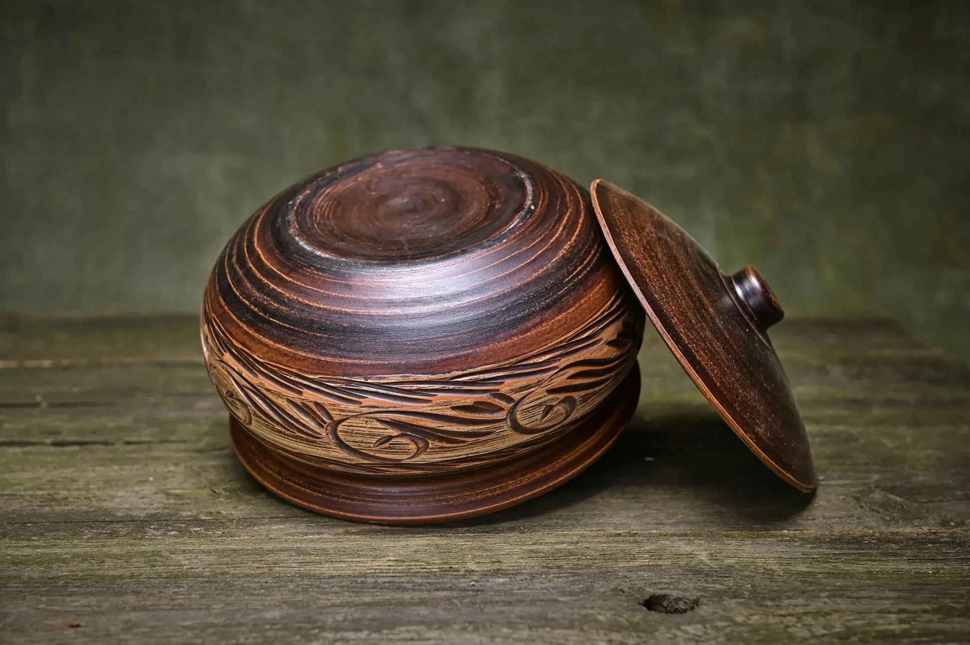 Handmade unglazed ceramic pot with etched design and lid on rustic wood surface