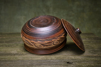 Handmade unglazed ceramic pot with etched design and lid on rustic wood surface