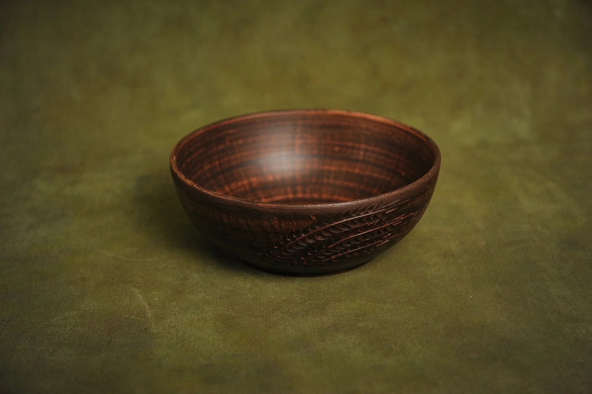 Handmade clay salad bowl with rustic engraved design on green background