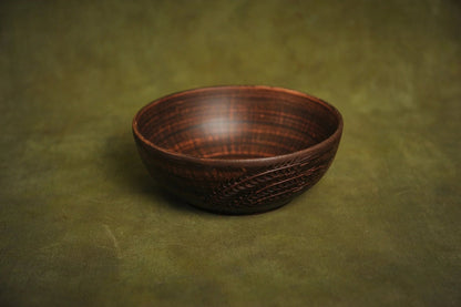 Handmade clay salad bowl with rustic engraved design on green background