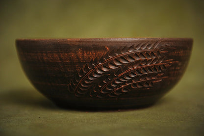 Handmade Ukrainian ceramic bowl with hand-engraved wheat design on rustic green background