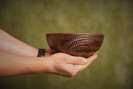 Hand holding a rustic handmade clay salad bowl with engraved wheat design, artisan pottery dinnerware