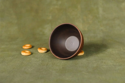 Handmade ceramic dipping bowl with brown finish on green background, artisan clay product