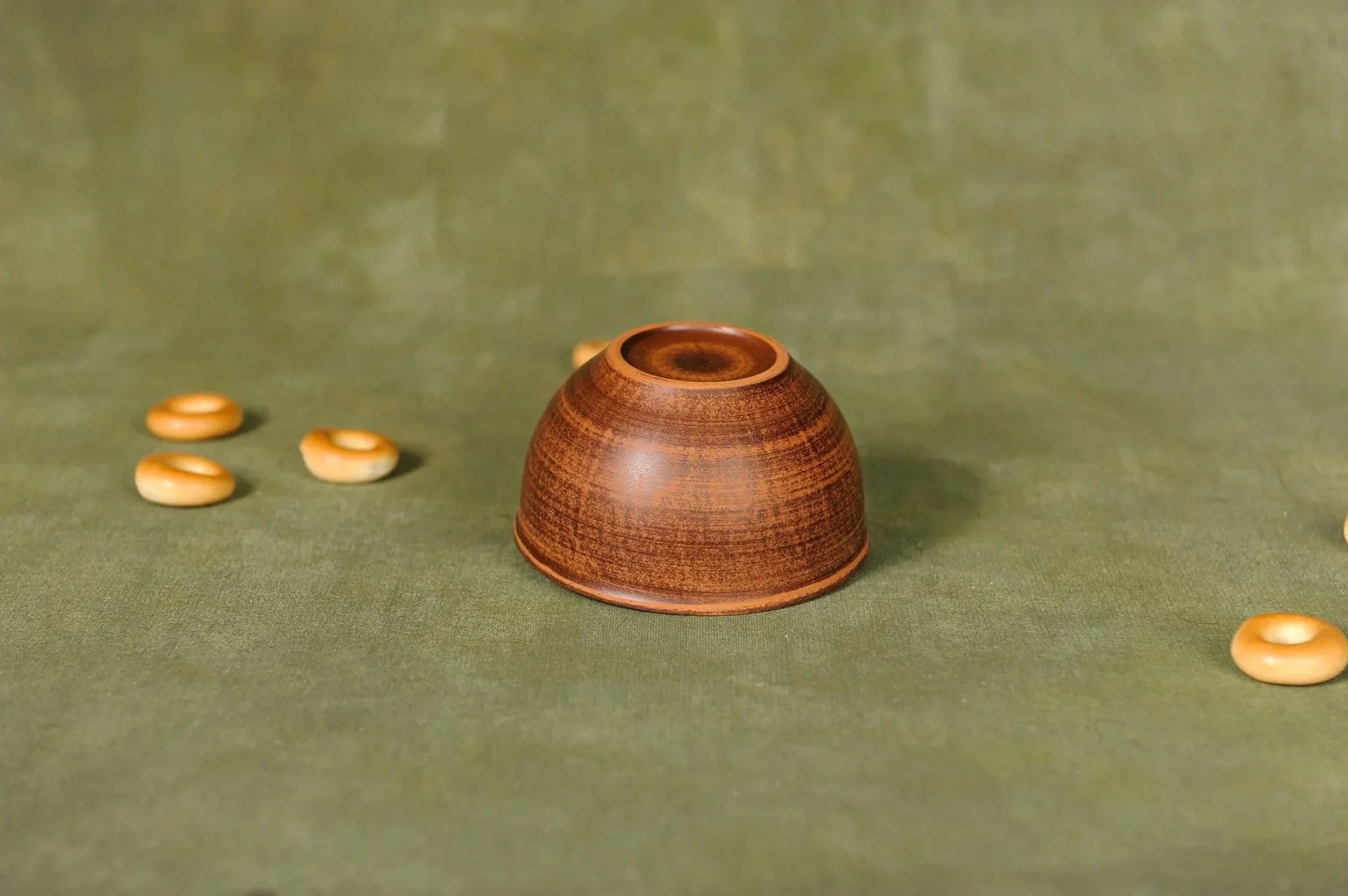 Handmade ceramic dipping bowl upside down on olive green cloth with small round beads