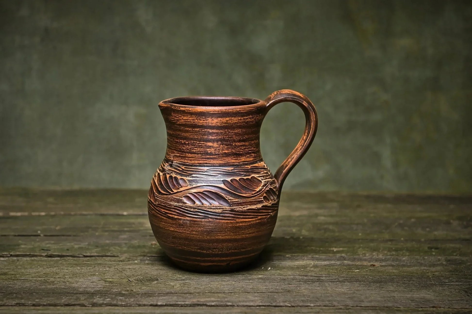 Handmade clay ceramic jug with carved leaf patterns, rustic pottery creamer on wood table