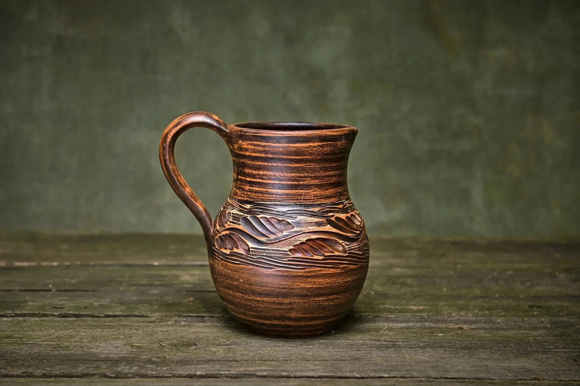 Handmade clay ceramic jug with carved leaf design on rustic wooden table