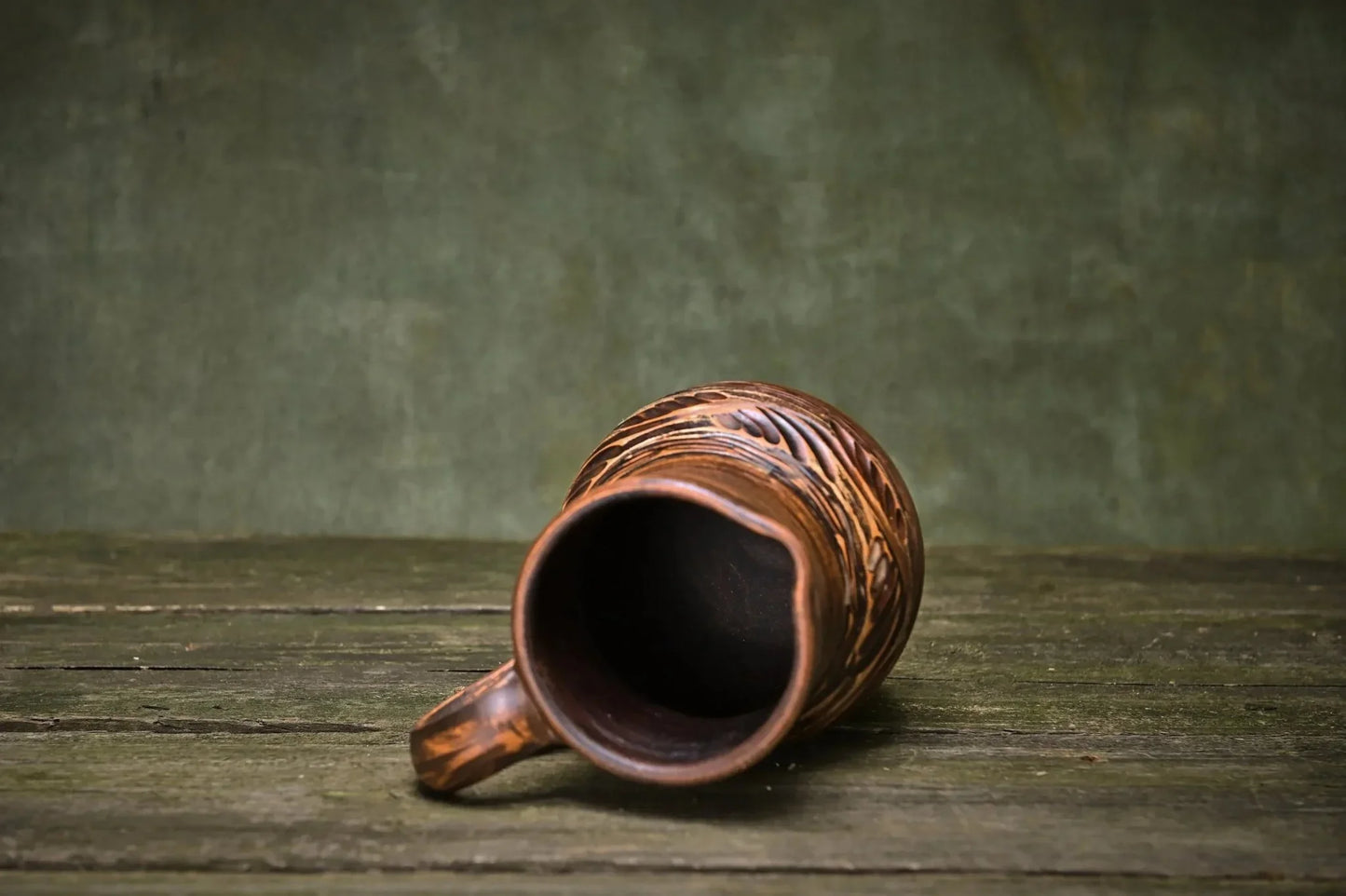 Handmade ceramic clay jug with carved patterns on rustic wooden surface