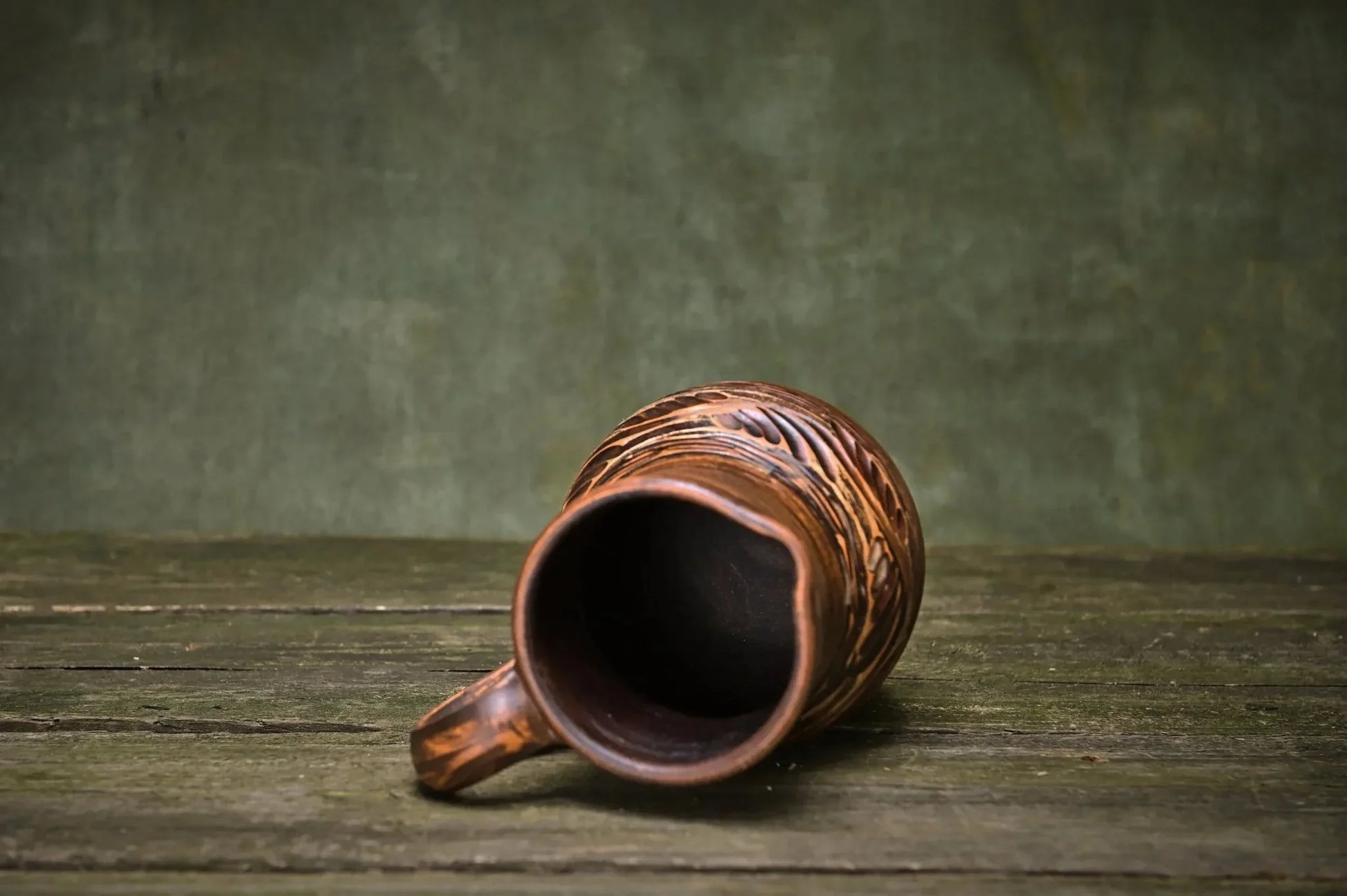Handmade ceramic clay jug with carved patterns on rustic wooden surface