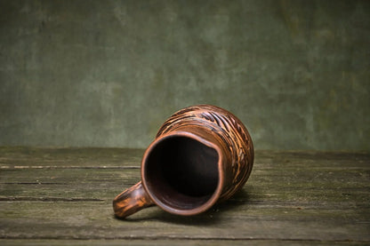 Handmade ceramic clay jug with carved patterns on rustic wooden surface