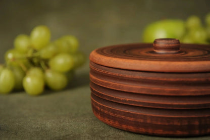 Handmade ceramic clay pot with lid, rustic design, grapes in background, artisan homeware