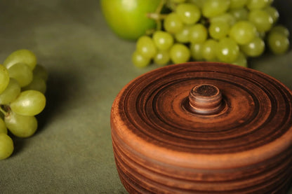 Handmade clay spice pot with lid on green fabric, grapes and apple in background