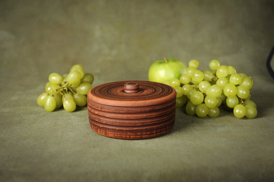 Handmade ceramic small clay pot with lid, rustic design, surrounded by green grapes and apple.