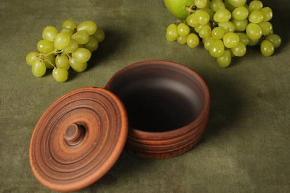 Handmade clay pot with lid on green cloth, surrounded by green grapes, rustic style