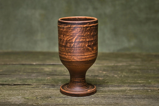 Handmade brown ceramic wine goblet on rustic wooden surface, artisan clay stemware