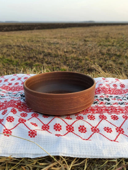 Handmade clay bowl on embroidered cloth, rustic outdoor setting, artisan earthenware homeware