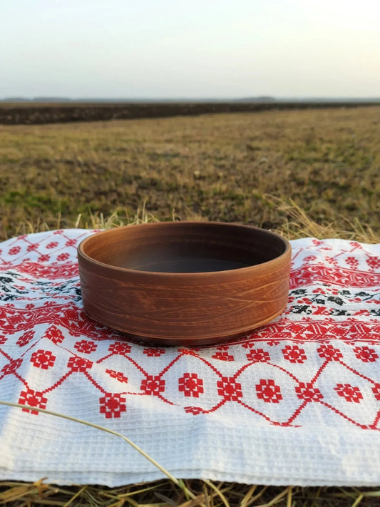Handmade rustic red clay bowl on embroidered cloth, outdoor setting, artisan pottery